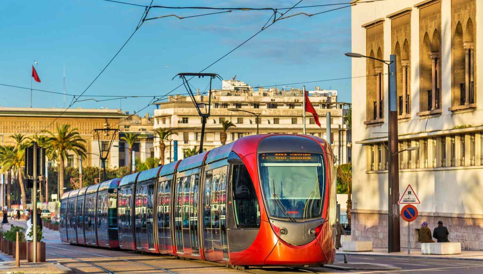 Modern red tram in the city center of Casablanca, Morocco, surrounded by palm trees and colonial architecture.
