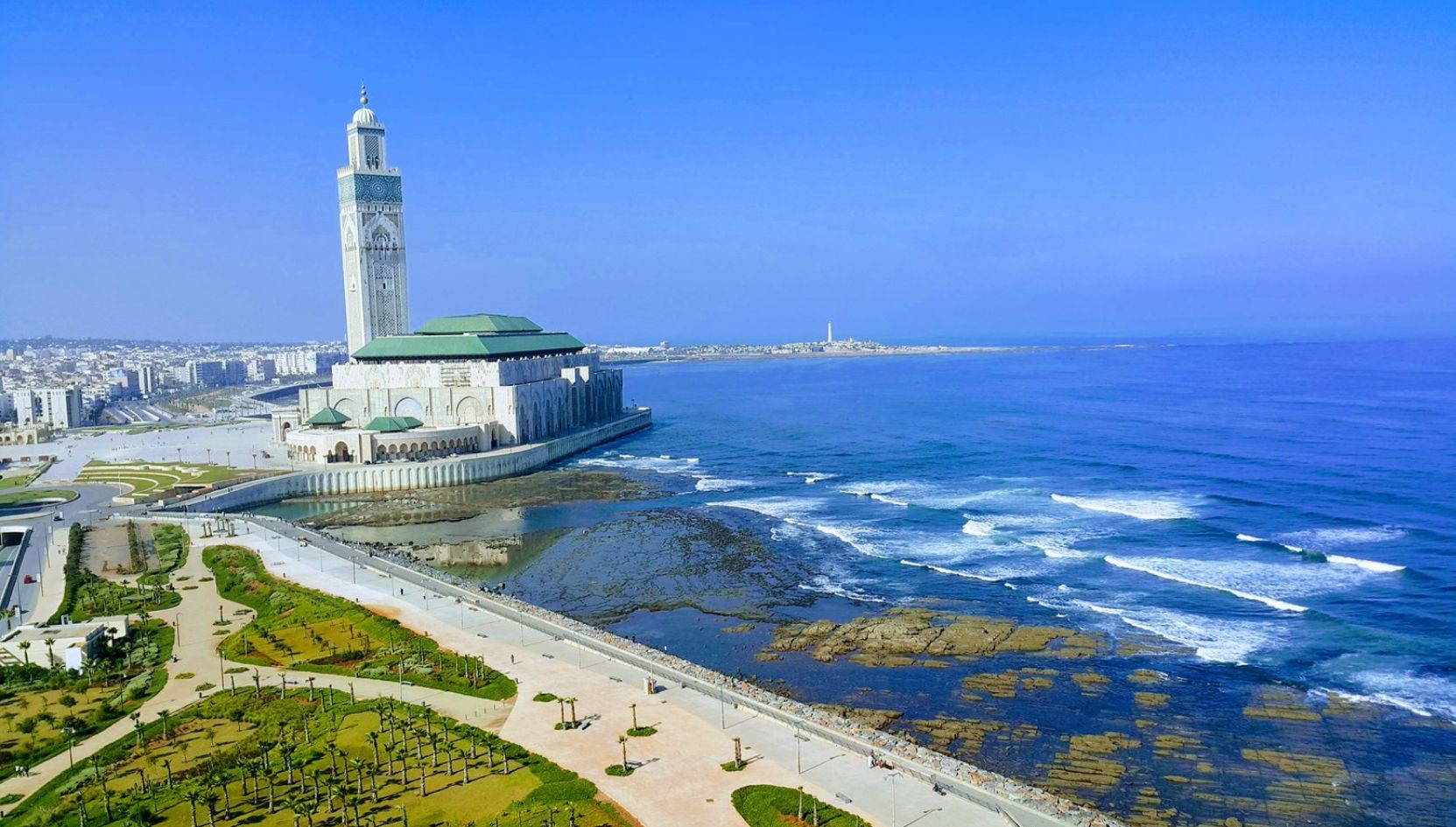 Aerial view of the Hassan II Mosque in Casablanca, Morocco, beside the Atlantic Ocean on a bright blue day.