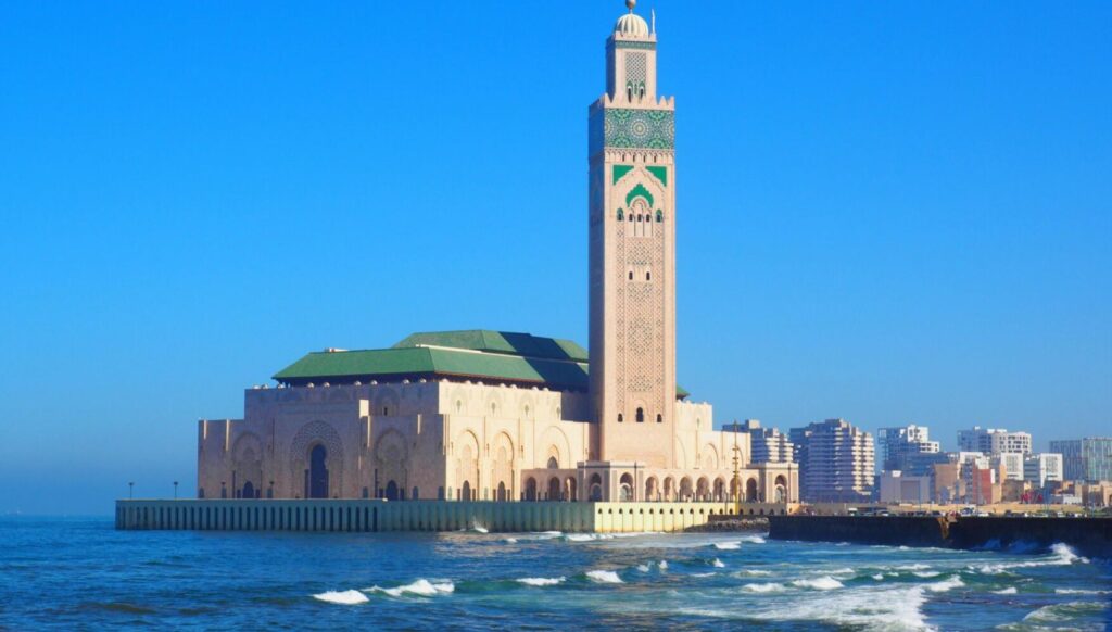 Hassan II Mosque in Casablanca, Morocco, standing by the Atlantic Ocean under a clear blue sky.