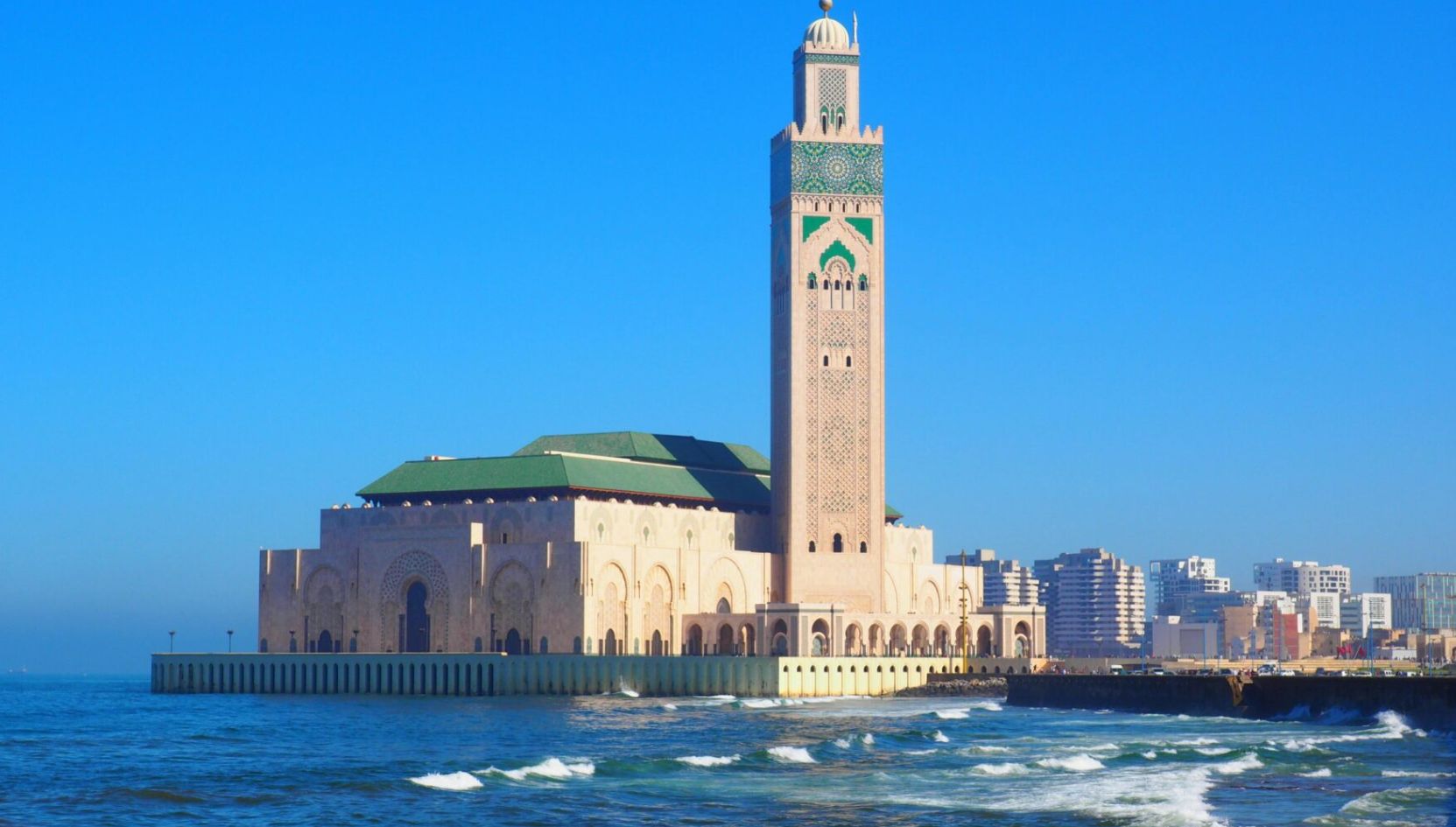 Hassan II Mosque in Casablanca, Morocco, standing by the Atlantic Ocean under a clear blue sky.