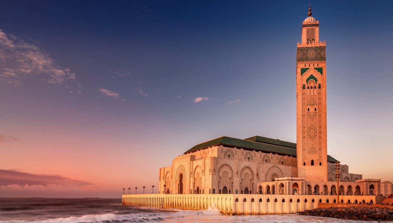 Hassan II Mosque in Casablanca, Morocco, illuminated by the warm light of sunset beside the Atlantic Ocean.