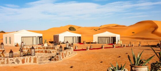 Luxury desert camp with white tents in the golden dunes of Erg Chebbi, Merzouga, Morocco.