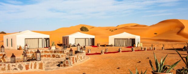 Luxury desert camp with white tents in the golden dunes of Erg Chebbi, Merzouga, Morocco.