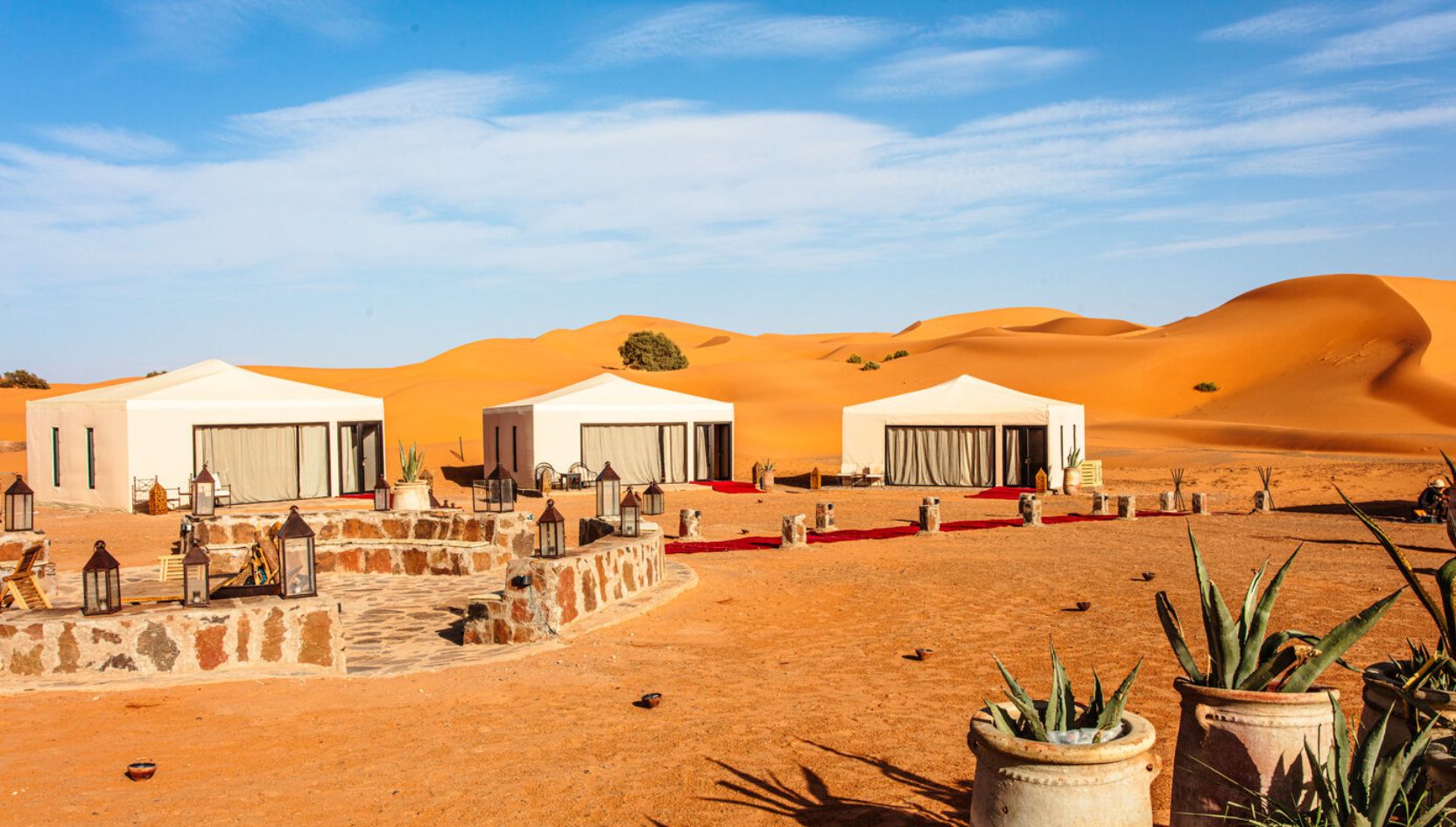 Luxury desert camp with white tents in the golden dunes of Erg Chebbi, Merzouga, Morocco.