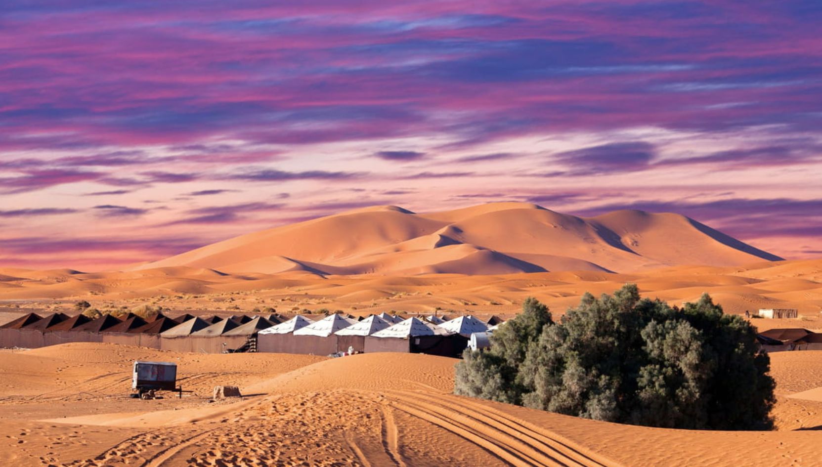 Luxury desert camp at sunset beneath the golden dunes of Erg Chebbi in Merzouga, Morocco.