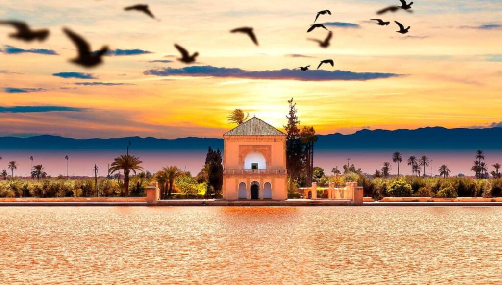 Sunset view of the Menara Gardens pavilion in Marrakech with birds flying over the lake