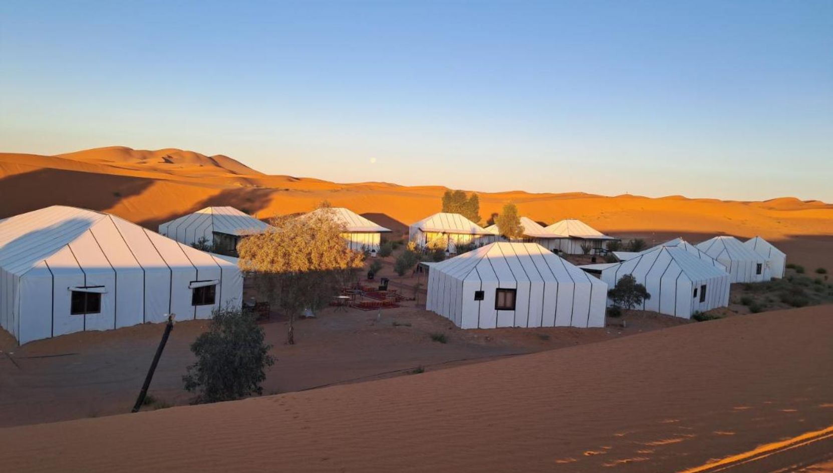 Luxury desert camp in Merzouga at sunset surrounded by golden dunes in the Moroccan Sahara.