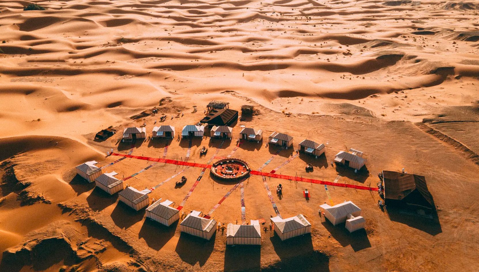 Aerial view of Merzouga Luxury Desert Camp arranged in a circular layout among the golden dunes of the Sahara Desert.