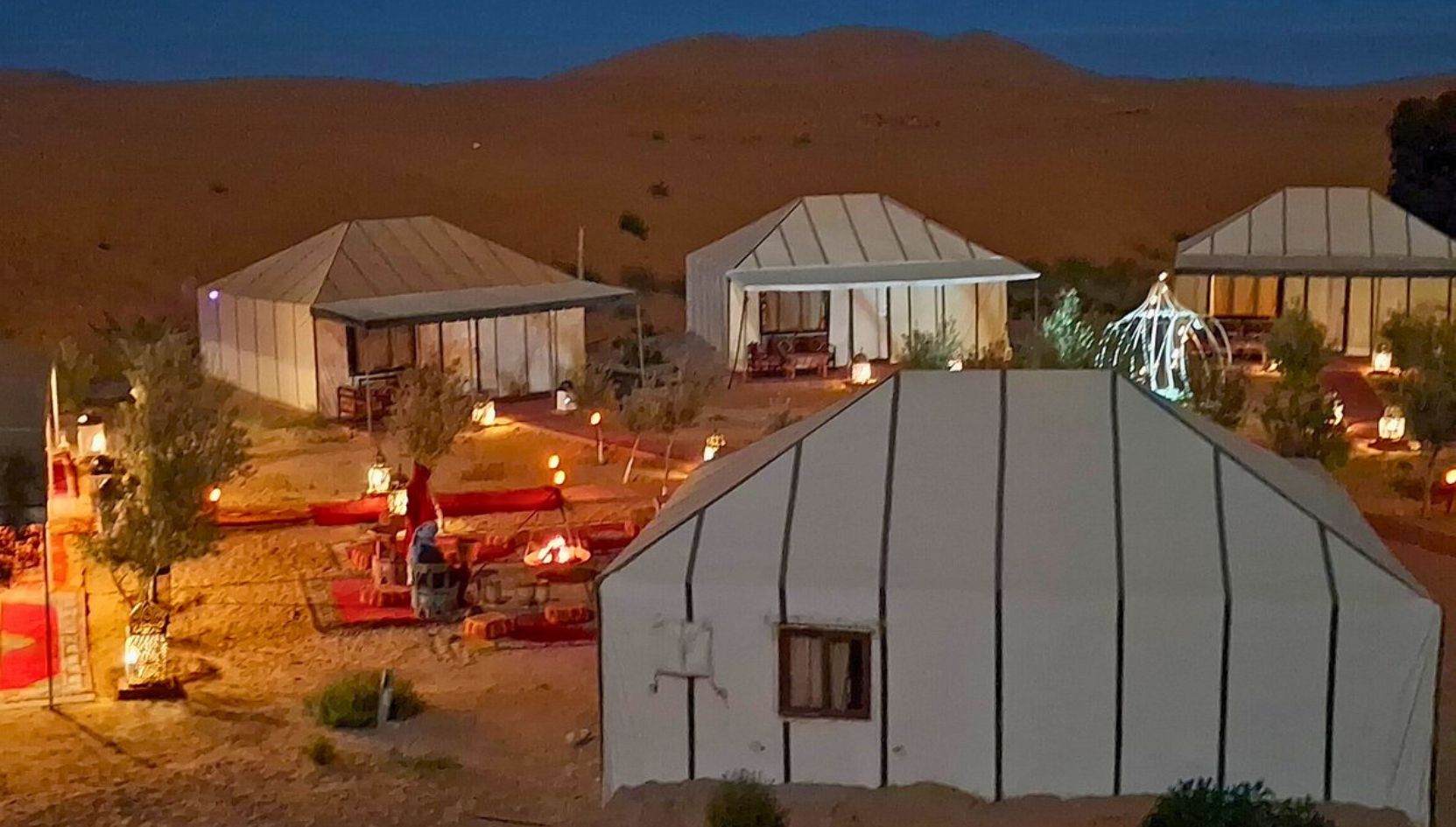 Night ambiance at Merzouga Luxury Desert Camp with glowing lanterns, tents, and cozy seating areas in the Sahara.