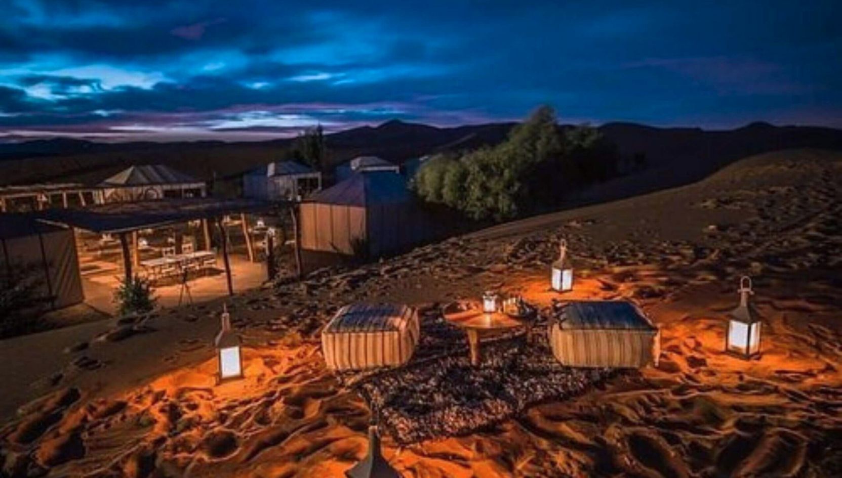 Night view of Merzouga Luxury Desert Camp with glowing lanterns and seating area under the Sahara sky.