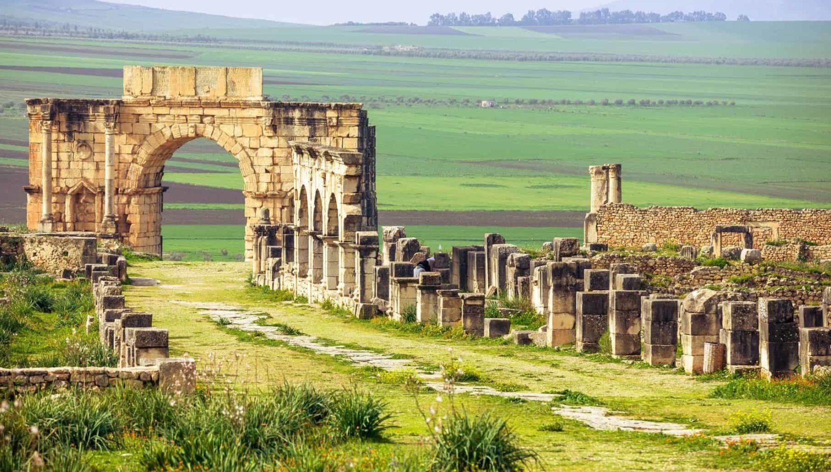 Ancient Roman ruins of Volubilis near Meknes, Morocco, featuring the Arch of Caracalla and green countryside.