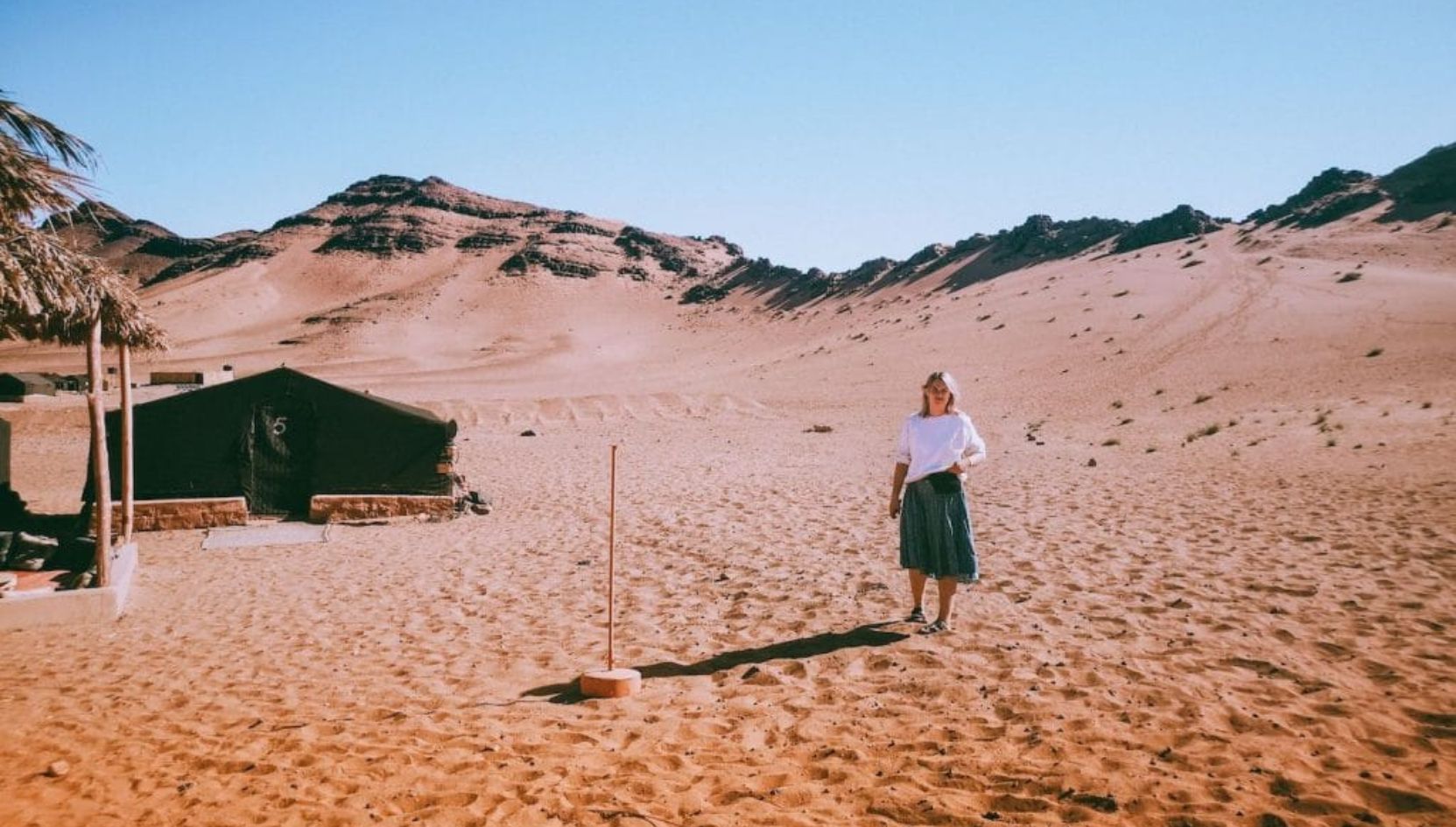 Traveler standing near a desert tent in Zagora surrounded by the golden dunes and rocky hills of the Sahara Desert.