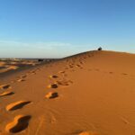 Footprints leading up a golden sand dune at sunrise in the Erg Chebbi desert near Merzouga, Morocco