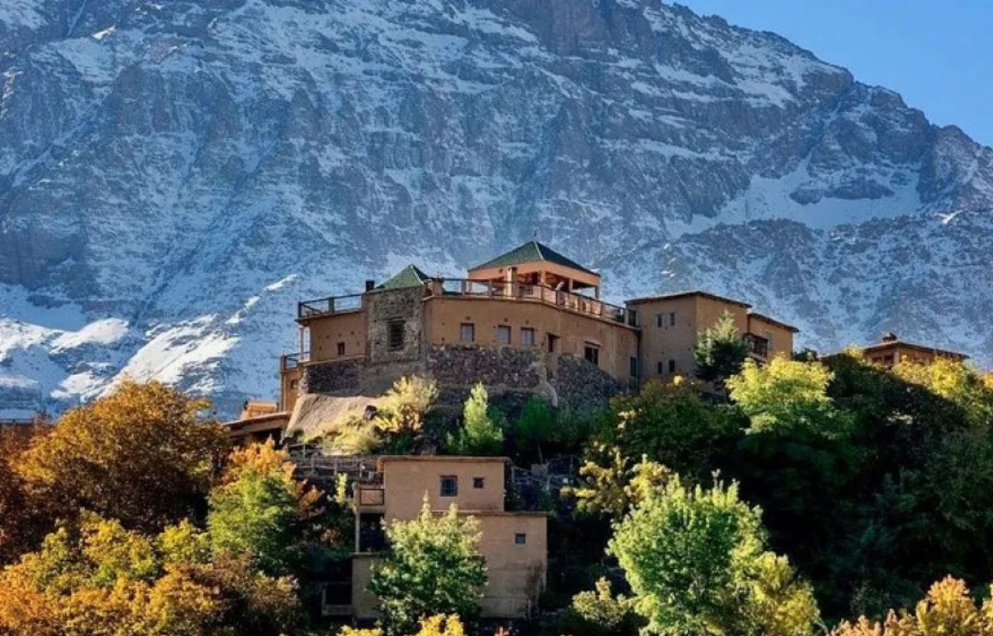 Berber village in the Atlas Mountains of Morocco with snow-covered peaks and green trees