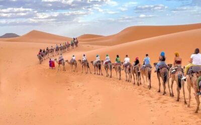 Camel caravan carrying travelers across the golden dunes of the Sahara Desert in Merzouga, Morocco.