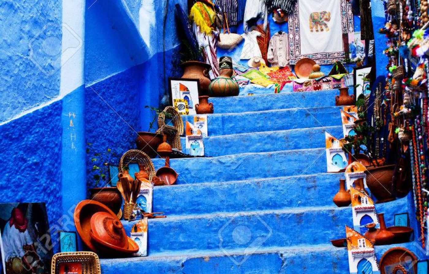 Blue painted stairs in Chefchaouen decorated with Moroccan handicrafts, pottery, baskets, and traditional artwork.