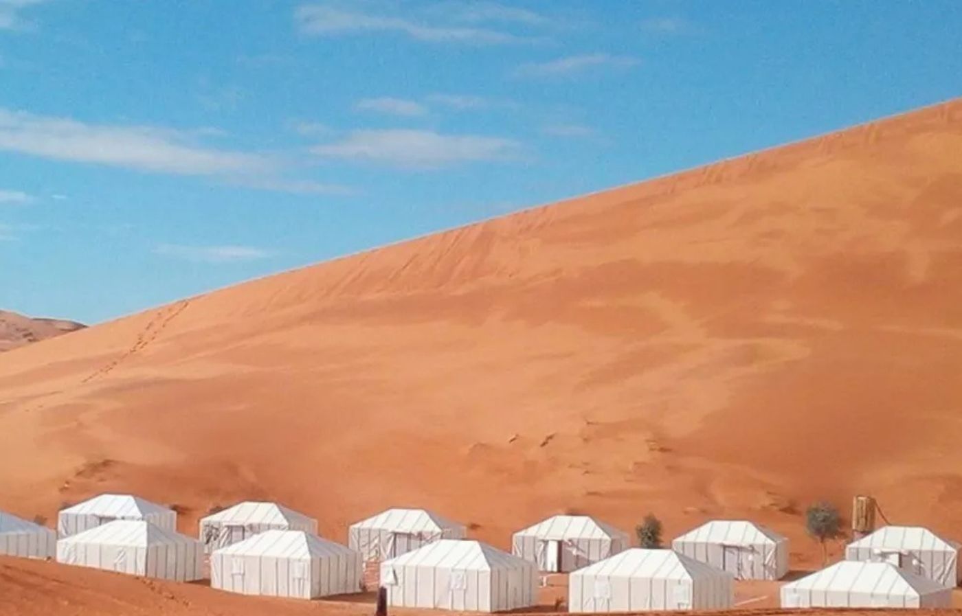 Luxury desert camp tents in the Merzouga Sahara dunes under a blue sky in Morocco
