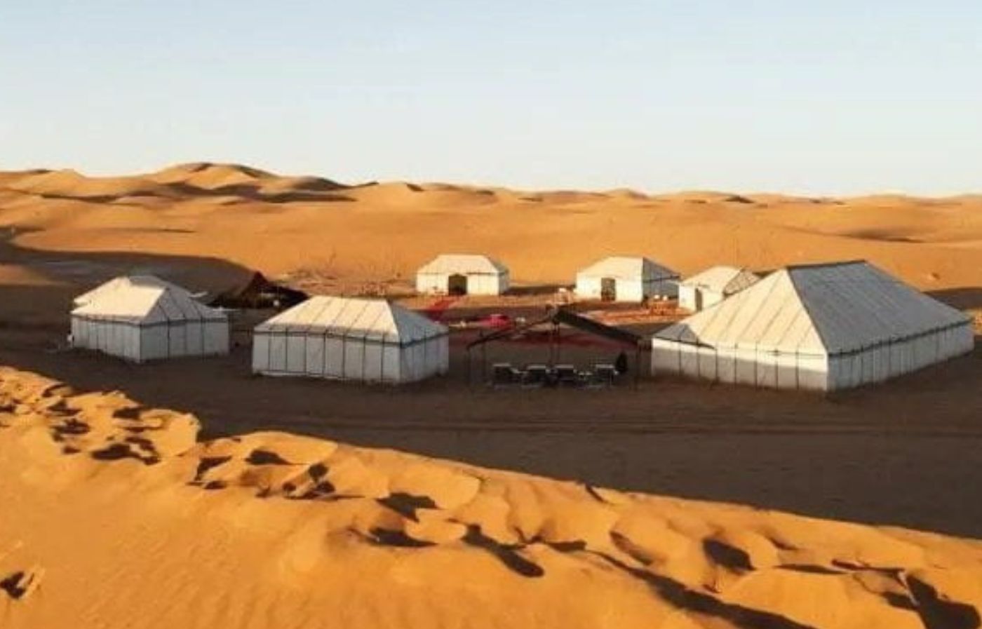 Luxury desert camp tents in the Merzouga Sahara surrounded by golden sand dunes at sunset