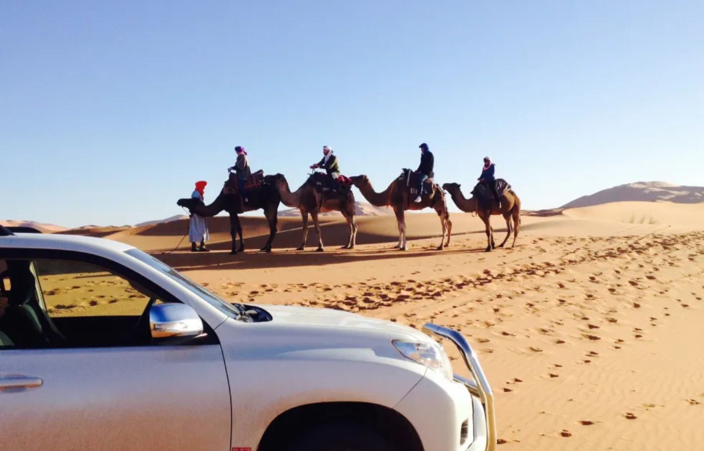 Camel caravan and 4x4 vehicle during a desert tour in the Merzouga Erg Chebbi dunes