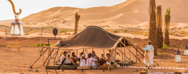 Group of travelers sitting under a Berber tent at a desert camp in Merzouga with sand dunes in the background