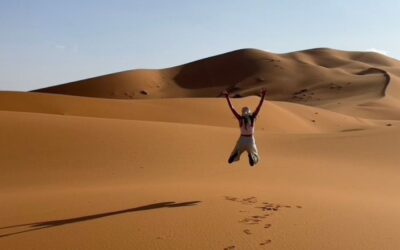 Traveler jumping in the golden sand dunes of Merzouga during a Sahara desert adventure in Morocco