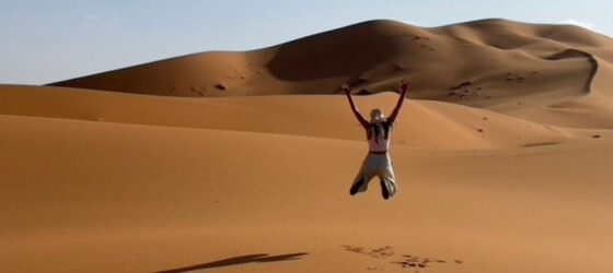 Traveler jumping in the golden sand dunes of Merzouga during a Sahara desert adventure in Morocco