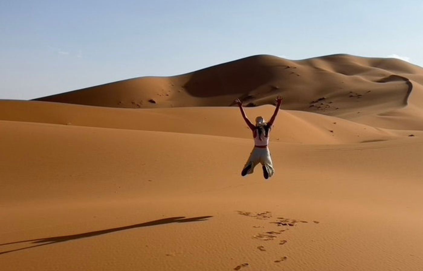 Traveler jumping in the golden sand dunes of Merzouga during a Sahara desert adventure in Morocco