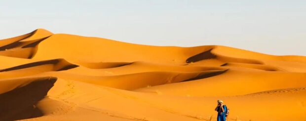 Berber man walking across the golden sand dunes of the Merzouga Sahara Desert in Morocco