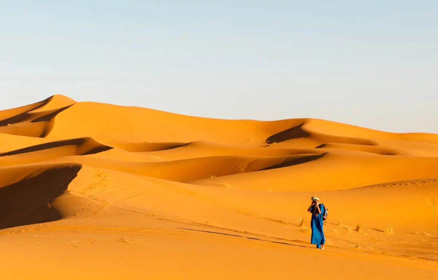 Berber man walking across the golden sand dunes of the Merzouga Sahara Desert in Morocco