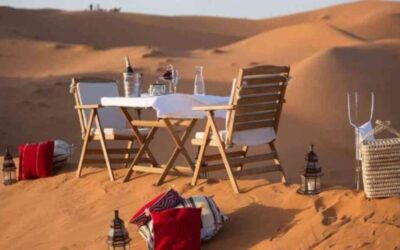 Romantic desert dinner setup with wooden chairs, table, lanterns, and cushions on the sand dunes of Merzouga in Morocco