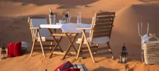 Romantic desert dinner setup with wooden chairs, table, lanterns, and cushions on the sand dunes of Merzouga in Morocco