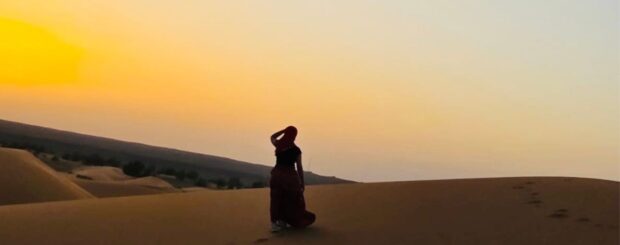 Woman walking alone on the sand dunes of the Merzouga desert at sunset in Morocco