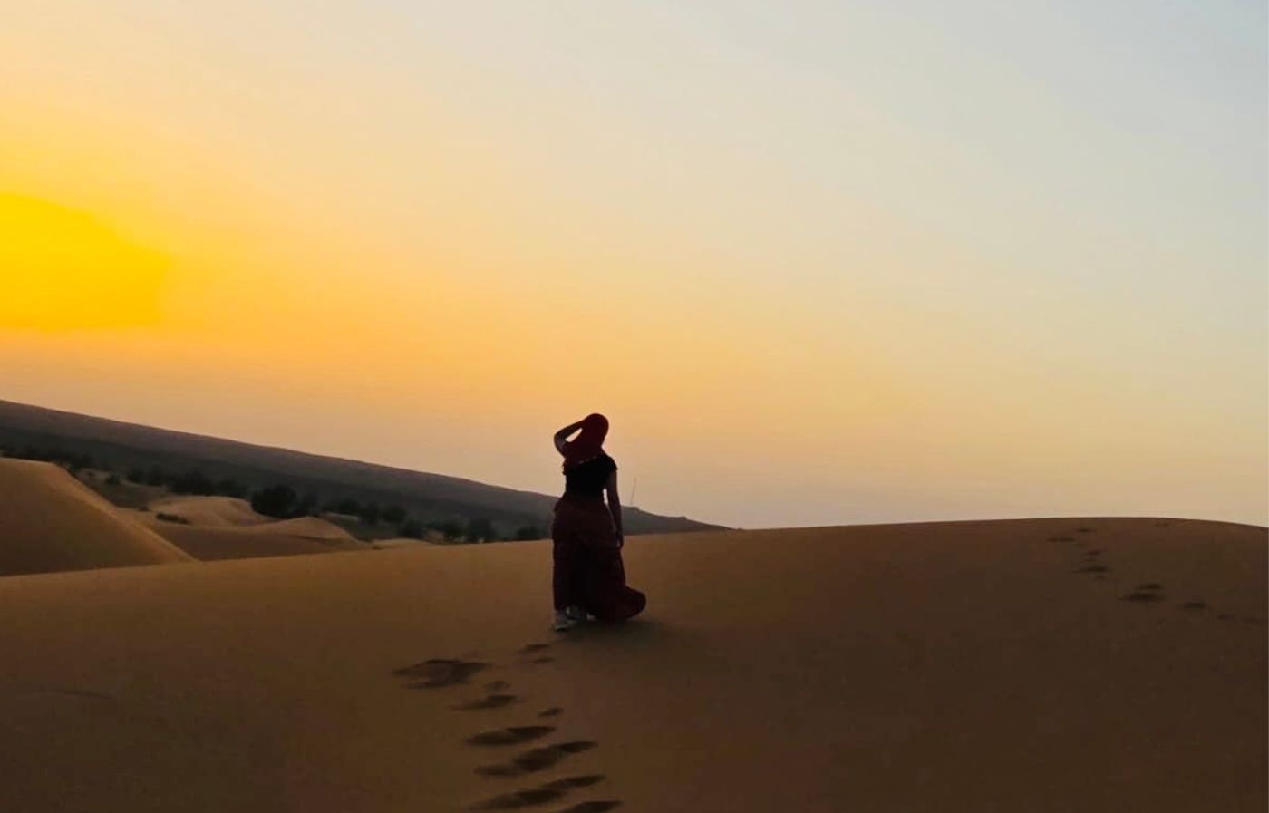Woman walking alone on the sand dunes of the Merzouga desert at sunset in Morocco