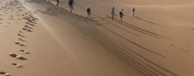 Group of tourists walking across the sand dunes of Merzouga during a Sahara desert trek in Morocco