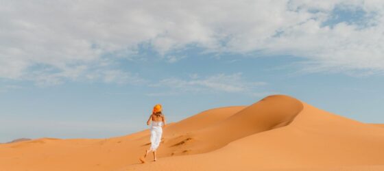 Woman walking on the sand dunes of Merzouga Sahara under a blue sky