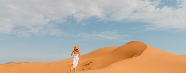 Woman walking on the sand dunes of Merzouga Sahara under a blue sky