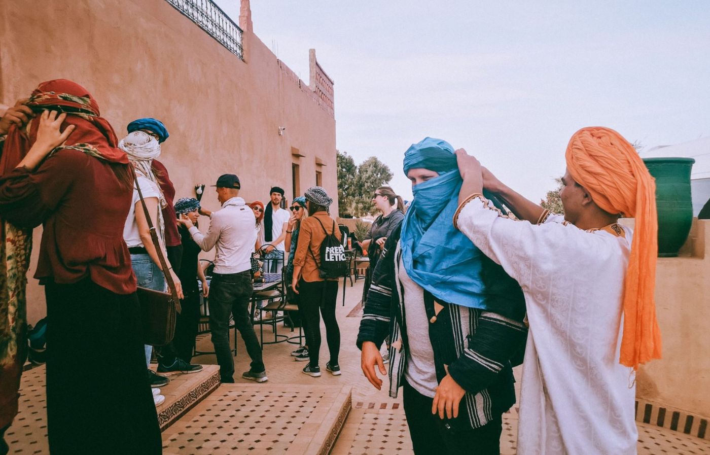 Local Moroccan guide helping travelers wear traditional desert scarves during a cultural experience in southern Morocco.