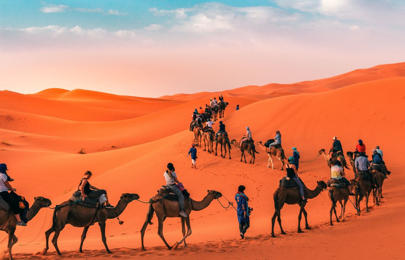 Camel caravan crossing the orange sand dunes of Erg Chebbi in the Sahara Desert, Morocco.