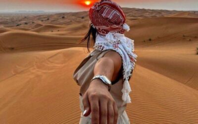 Traveler holding a companion’s hand while watching the sunset over the Sahara Desert sand dunes in Morocco.
