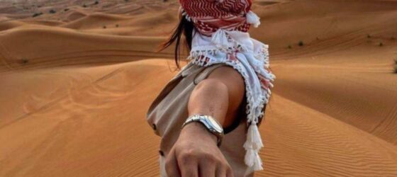 Traveler holding a companion’s hand while watching the sunset over the Sahara Desert sand dunes in Morocco.