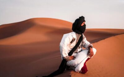 Saharan nomad wearing traditional desert clothing sitting on sand dunes in the Moroccan Sahara.