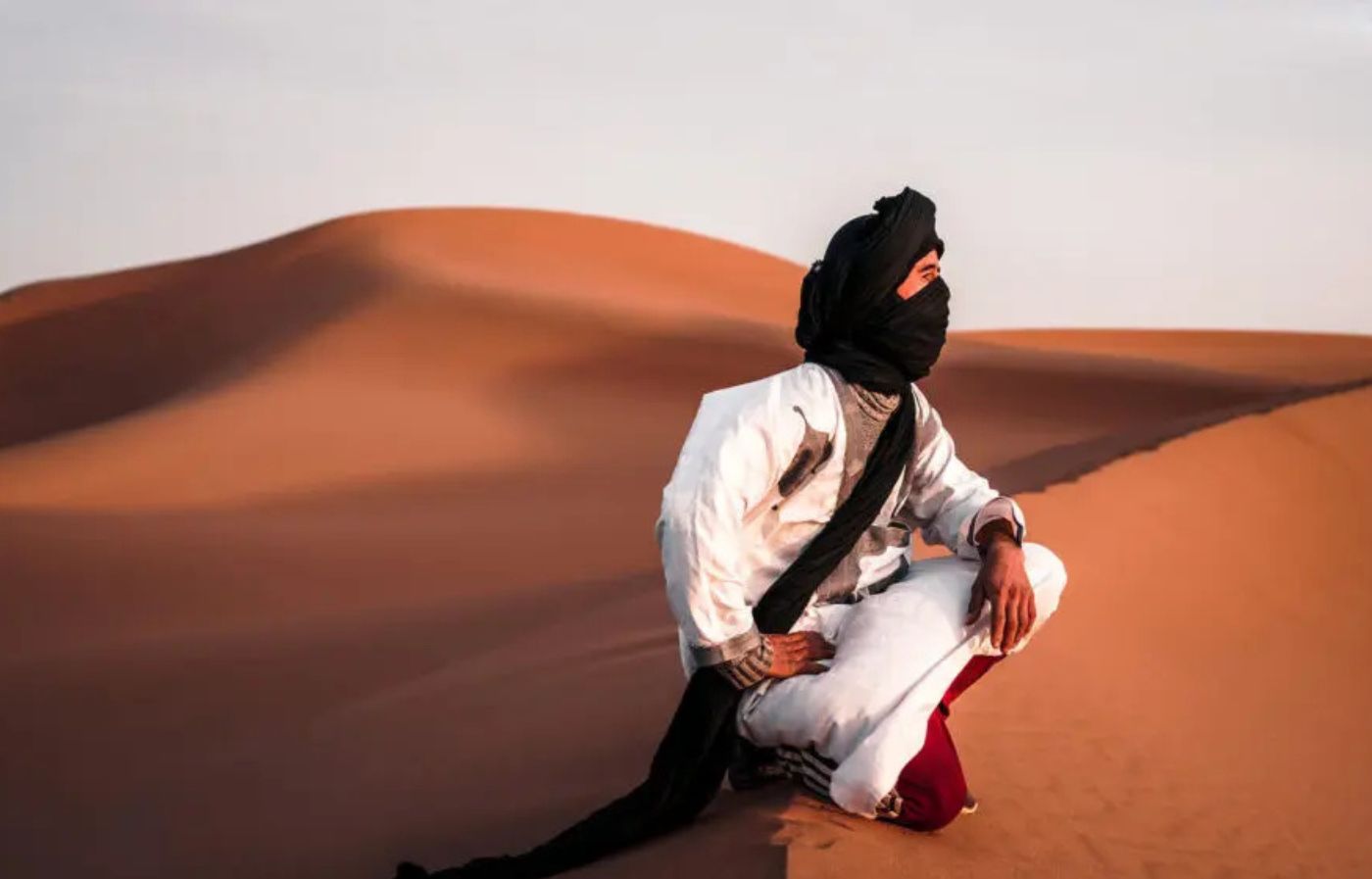 Saharan nomad wearing traditional desert clothing sitting on sand dunes in the Moroccan Sahara.