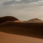 Golden sand dunes of the Sahara Desert at sunrise in Merzouga with soft shadows and cloudy sky