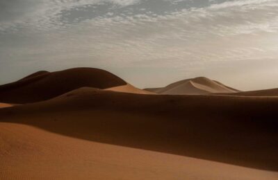Golden sand dunes of the Sahara Desert at sunrise in Merzouga with soft shadows and cloudy sky