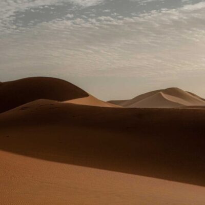 Golden sand dunes of the Sahara Desert at sunrise in Merzouga with soft shadows and cloudy sky