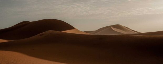 Golden sand dunes of the Sahara Desert at sunrise in Merzouga with soft shadows and cloudy sky
